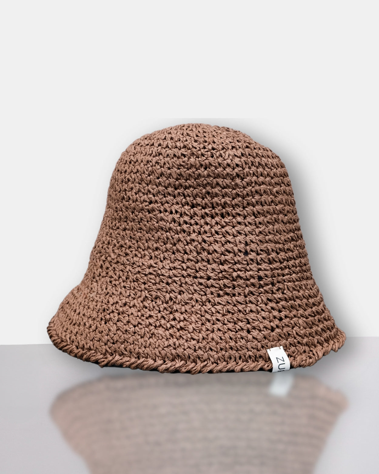 Brown knitted bucket hat on a white surface with a light gray background